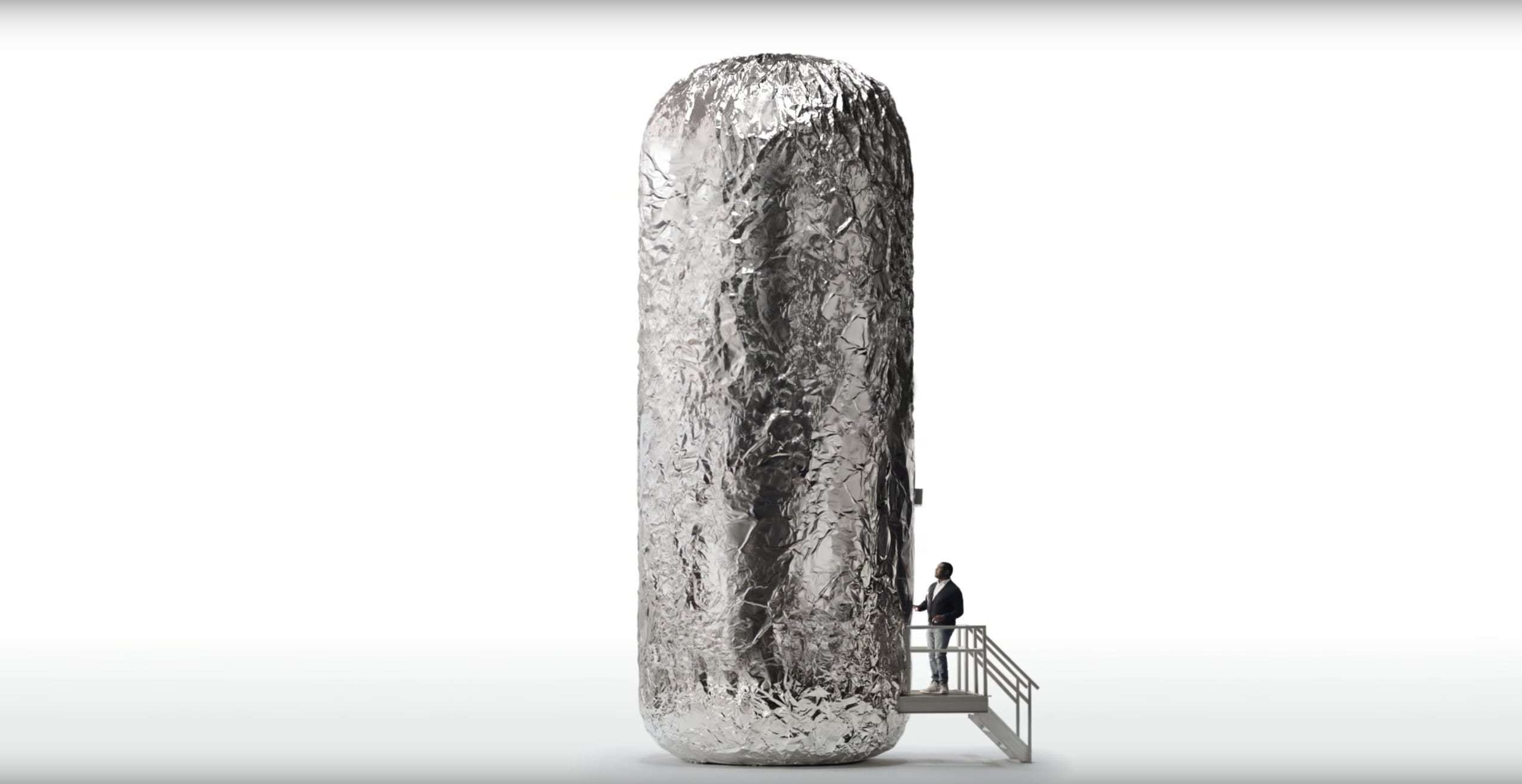 A man at a top of a small staircase looking up at a giant burrito.