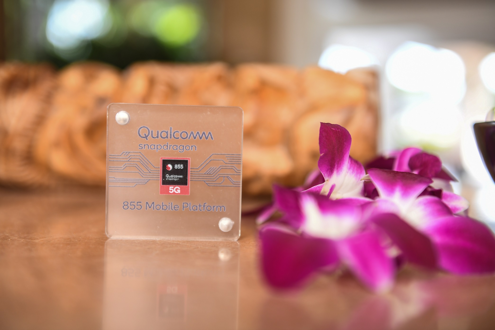 A Qualcomm Snapdragon chip next to a bunch of purple flowers.