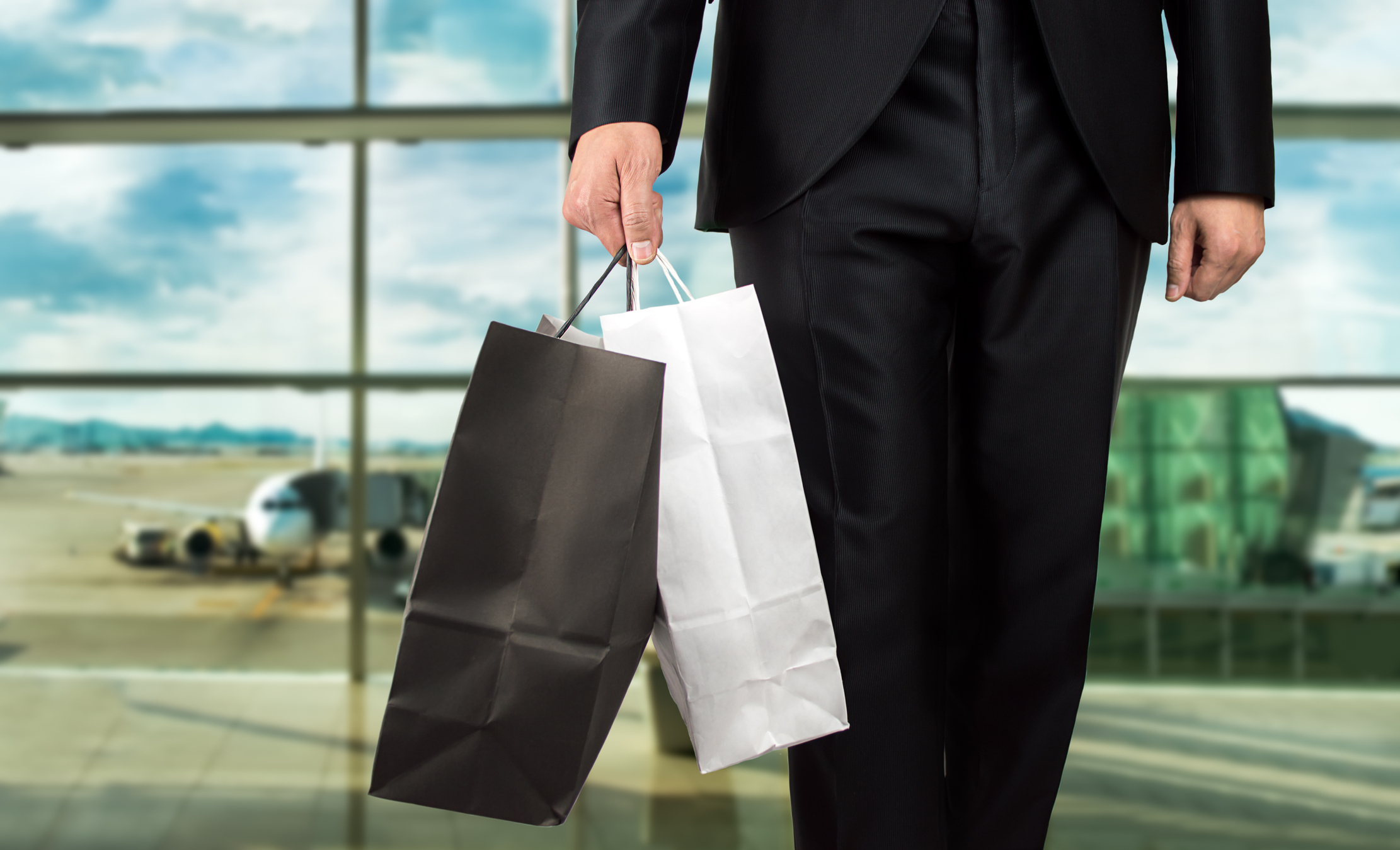 Man holding shopping bags in airport terminal.