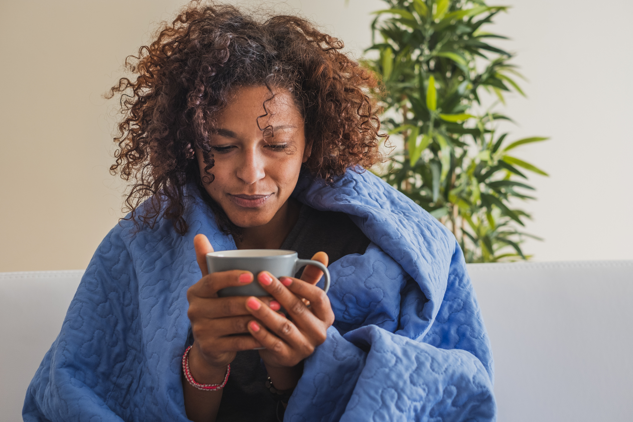 Woman wrapped in blanket holding a mug.