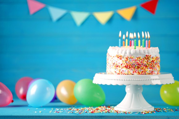 Birthday cake with lit candles and baloons in background.