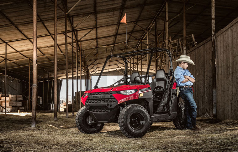 Young man in a Western hat leaning against a Ranger side-by-side inside a large barn