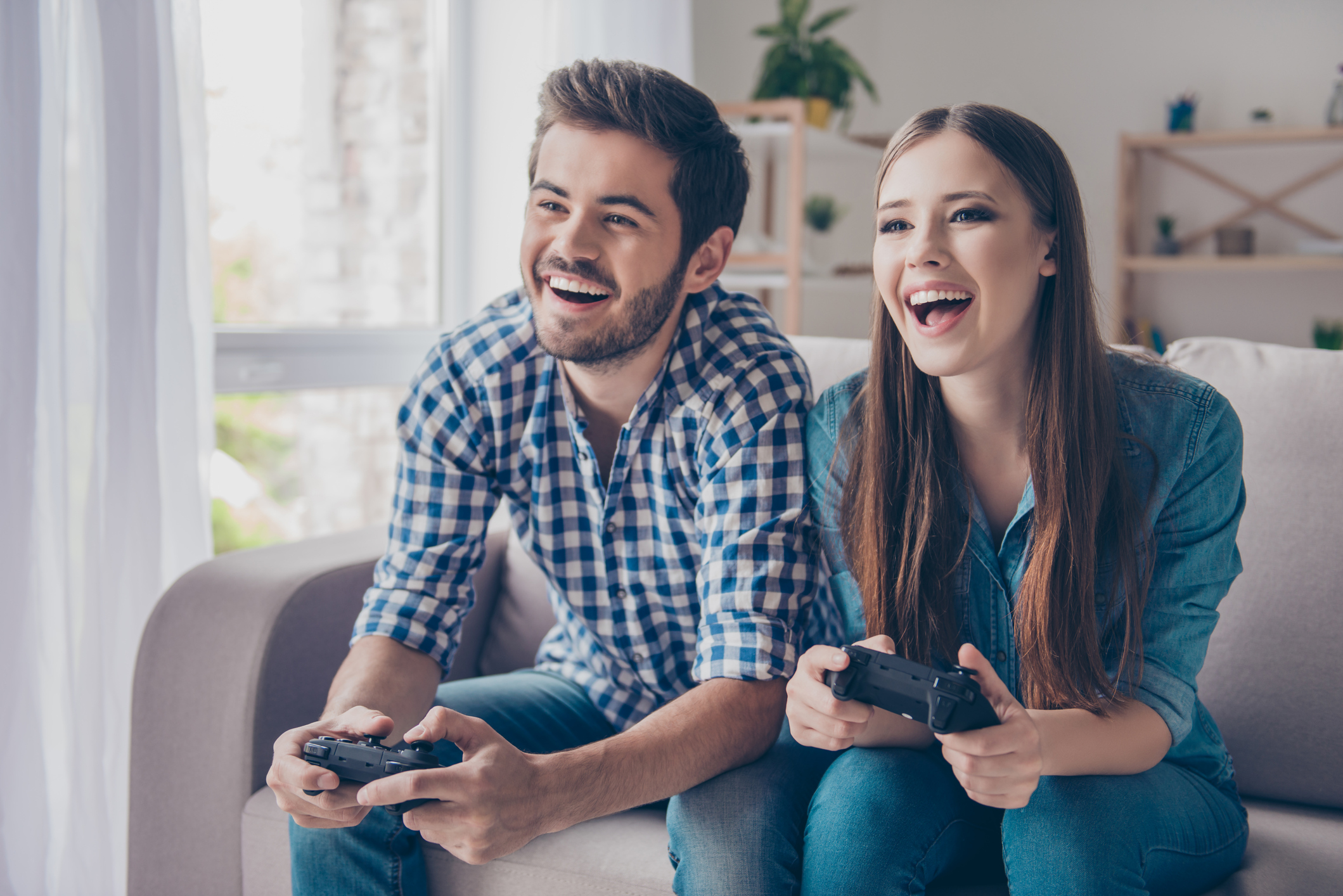 A young man and woman play a video game on the couch.