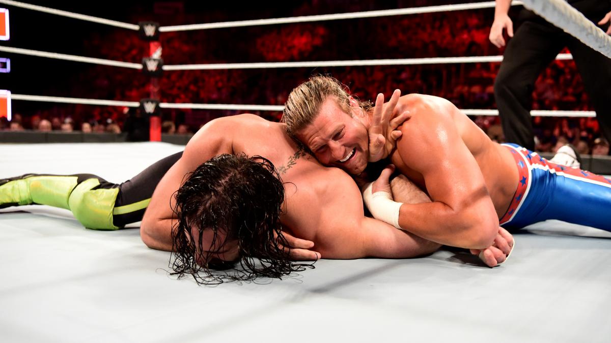 Two wrestlers facedown on a mat, with a referee in the background.