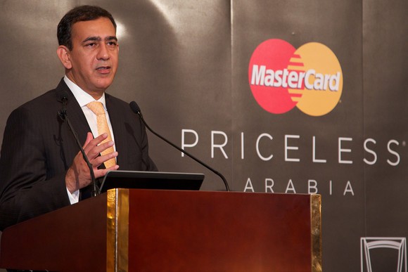 Man in a suit at podium next to Mastercard logo