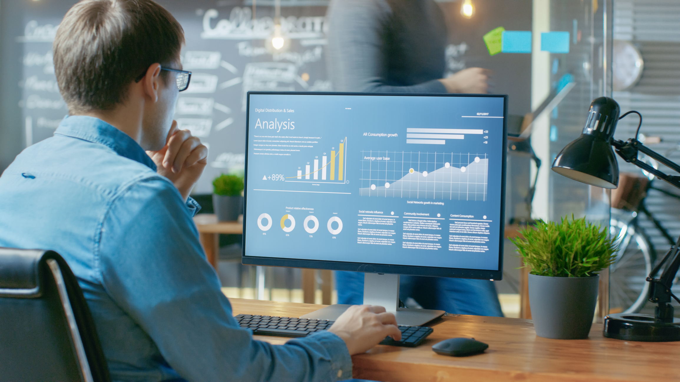 Sitting at a desk, a man looks at charts on a computer screen.