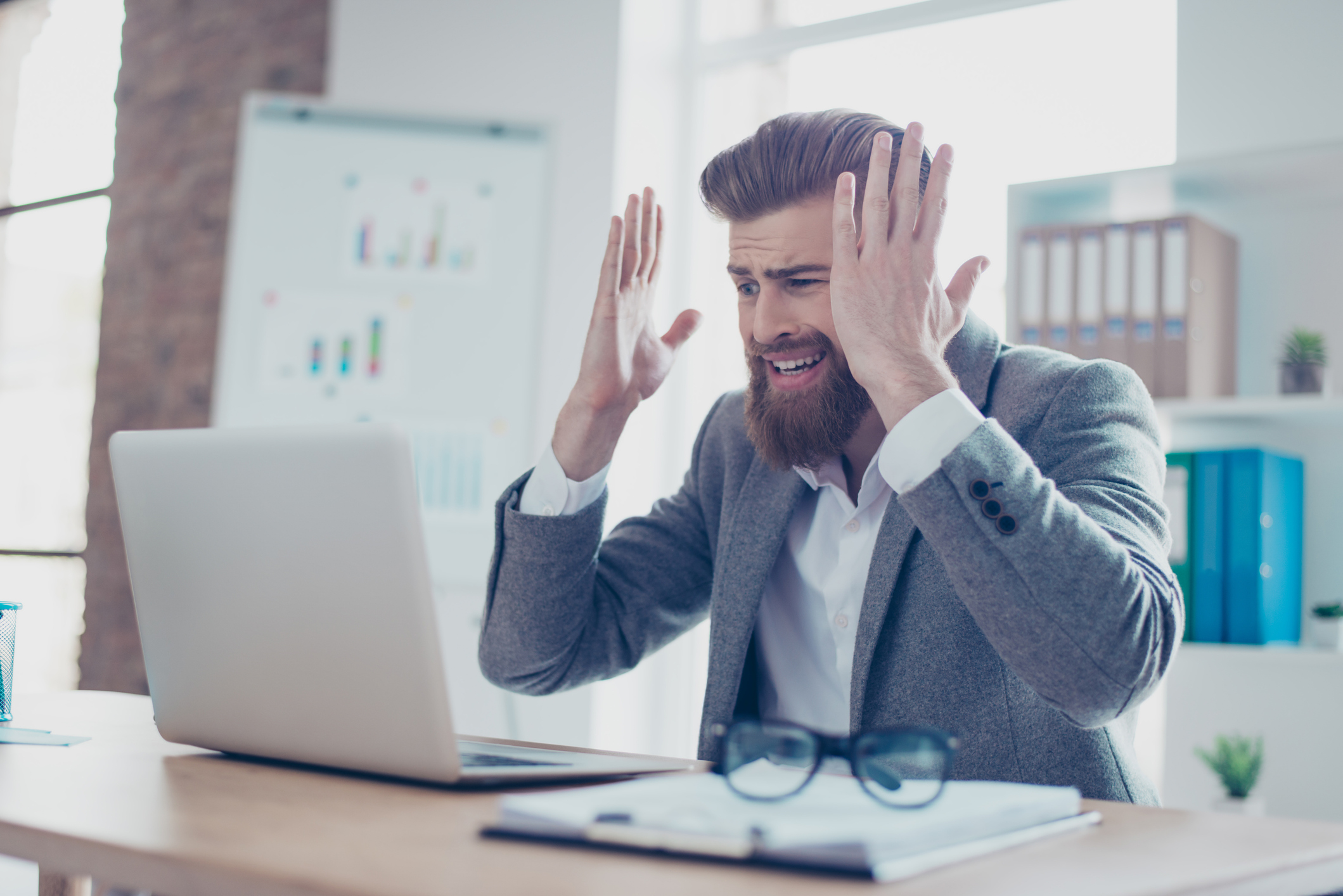 Man at laptop holding his hands up as if frustrated