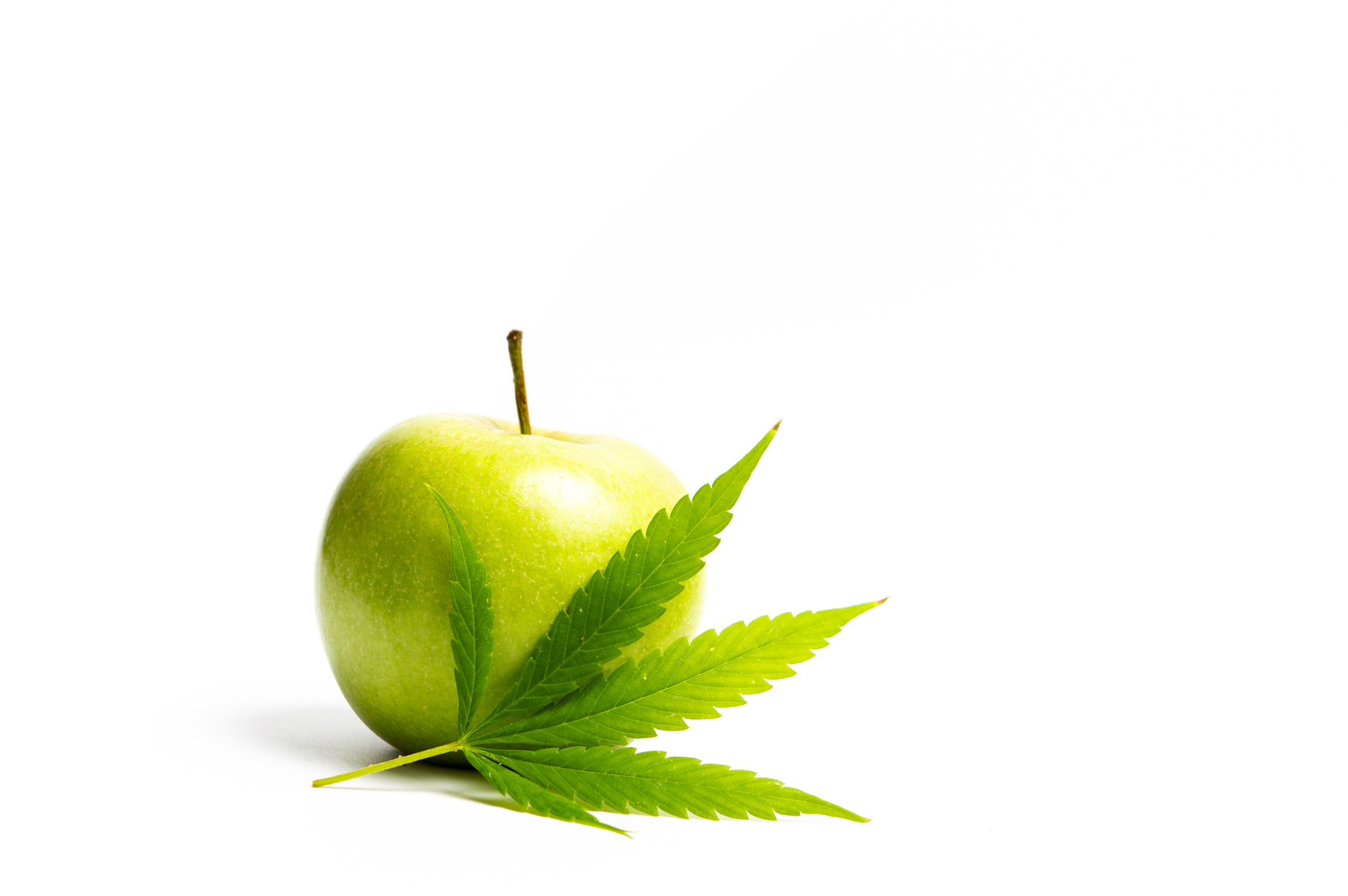 Marijuana leaf in front of a green apple.