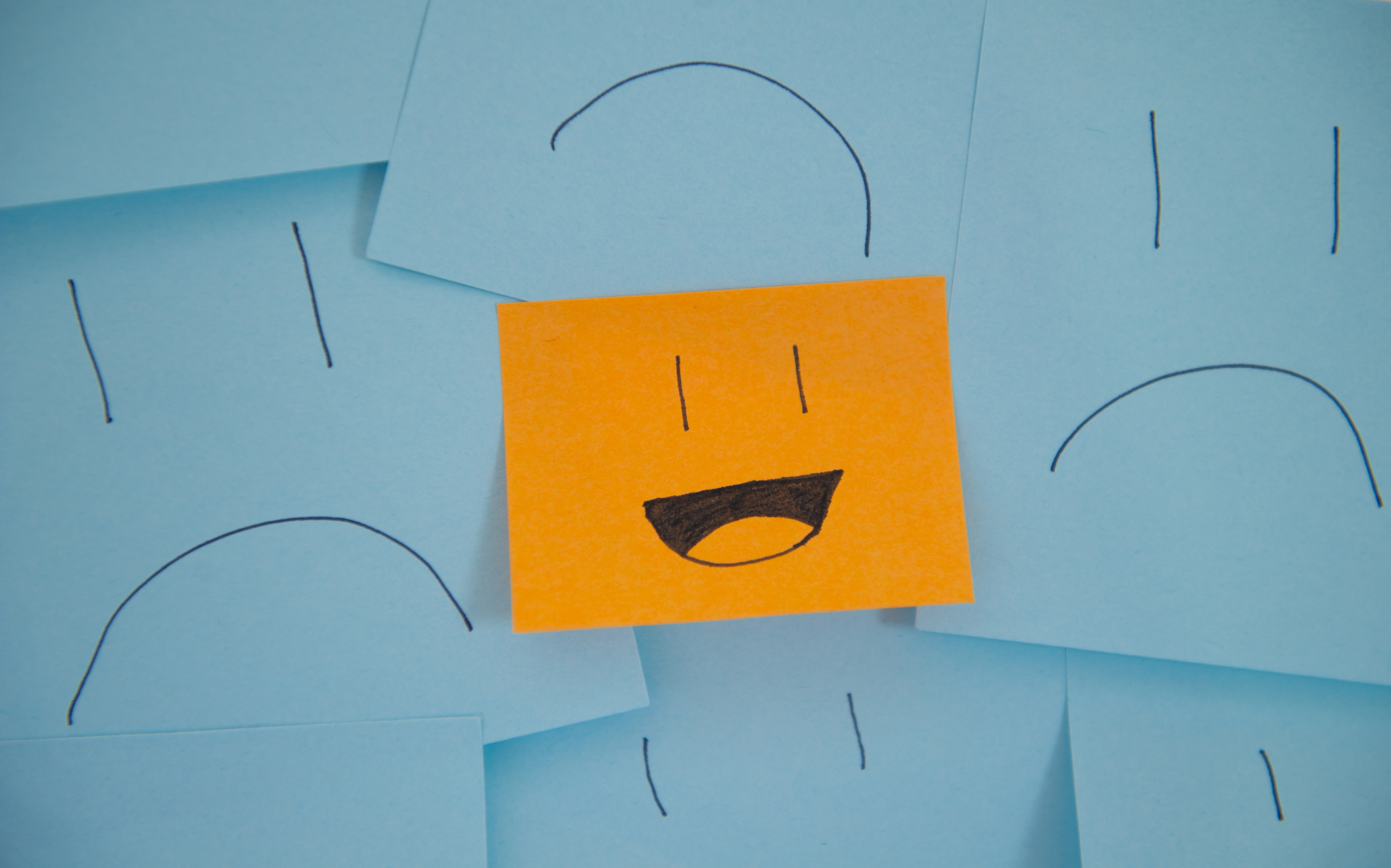 Orange sticky note with smiling face surrounded by blue sticky notes with frowning faces.