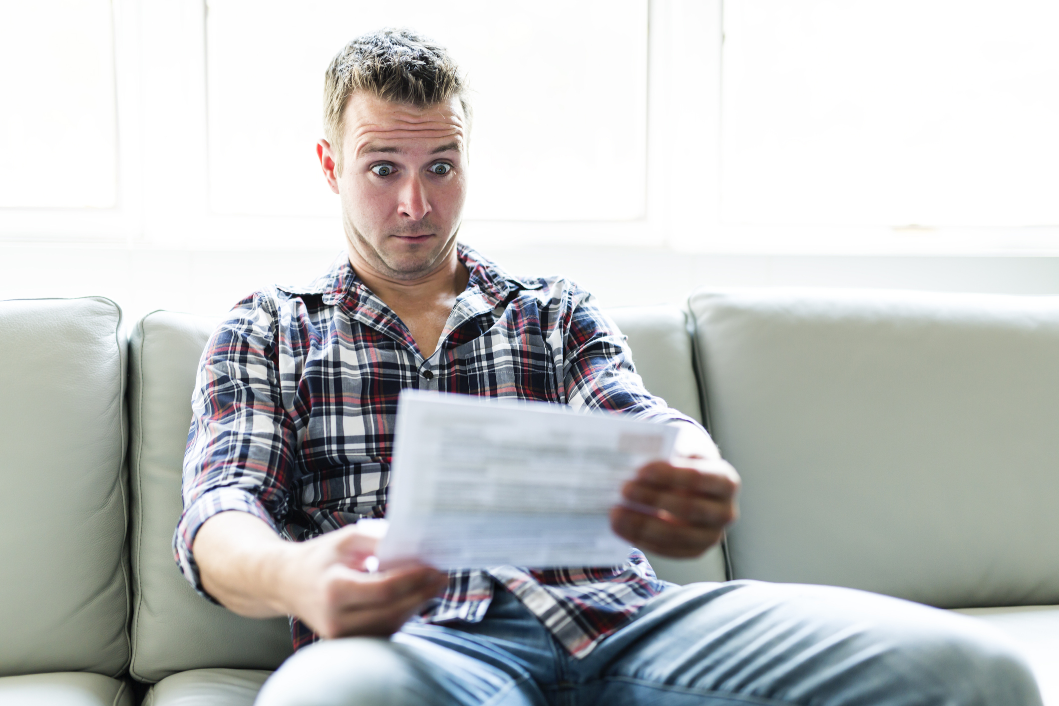 A man staring at a document with a shocked expression while sitting on a sofa.