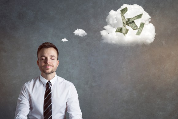 A man in a shirt and tie with a dream cloud above his head filled with money.
