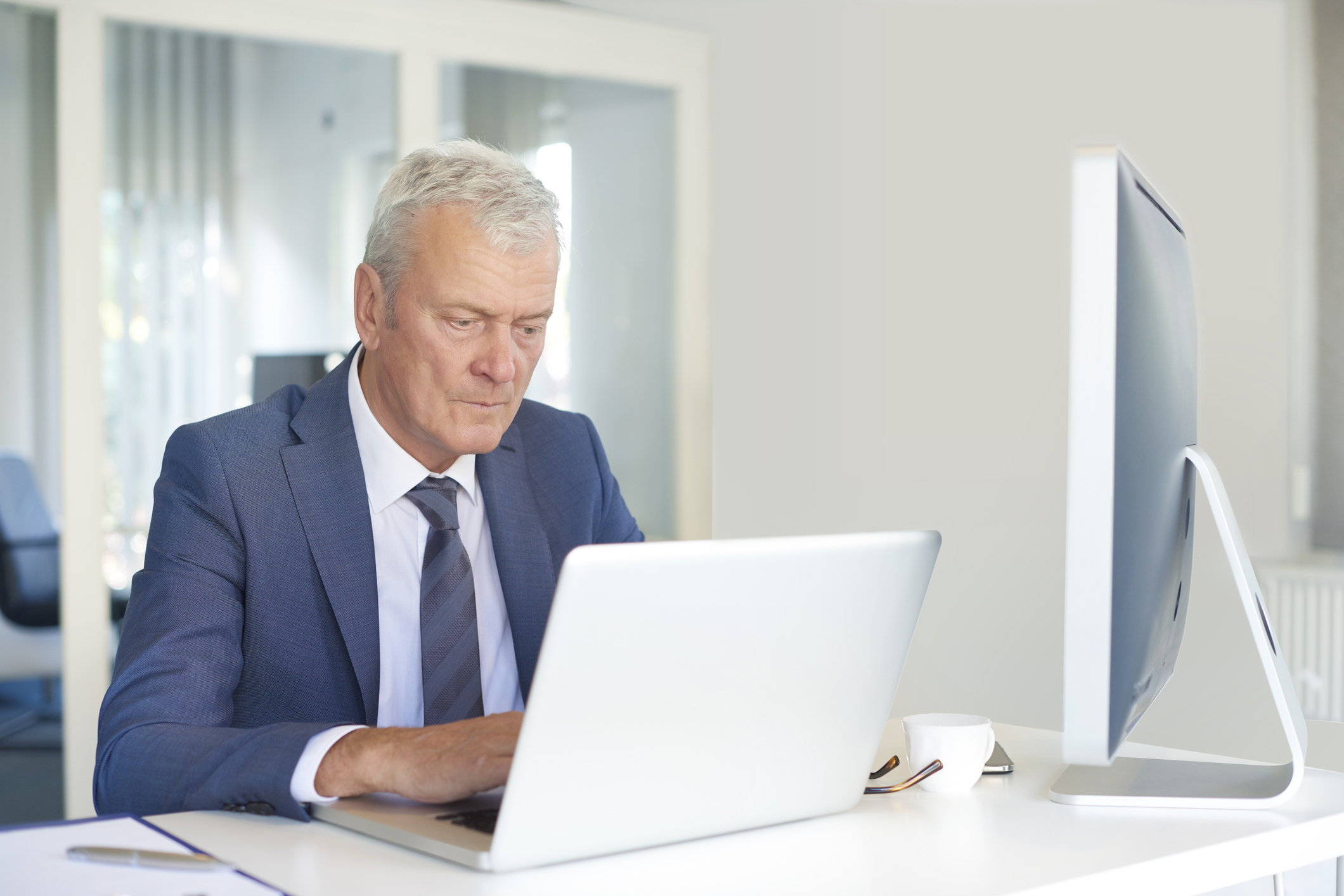 Older man in suit at a laptop.