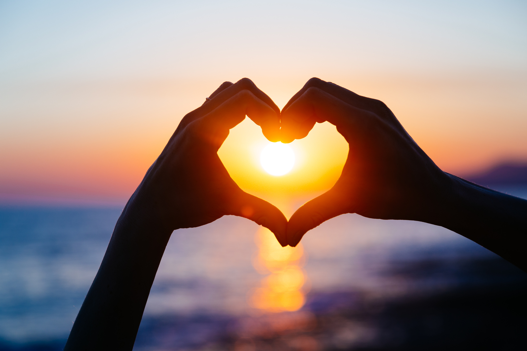 Fingers forming a heart shape with a sunset in the background.
