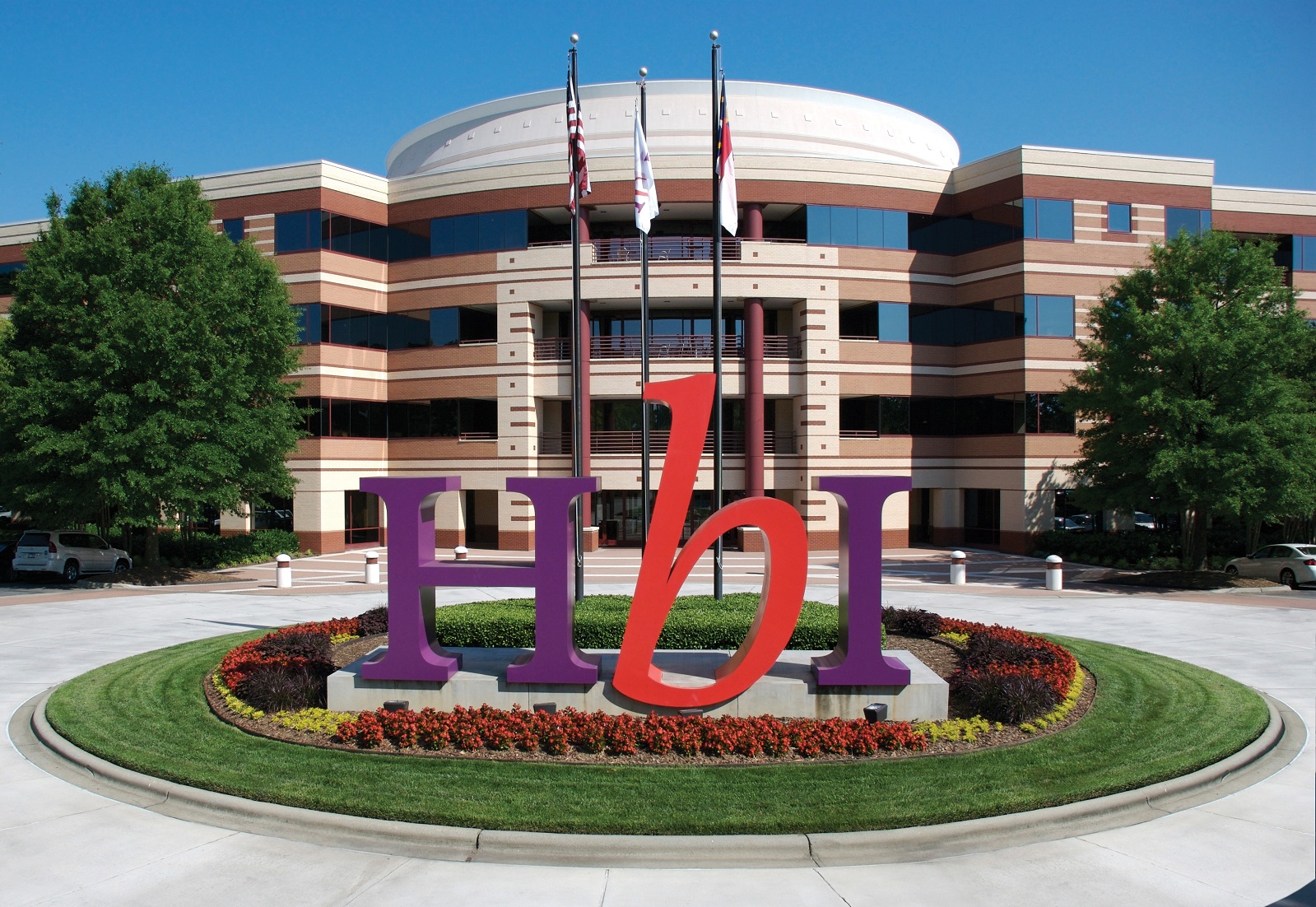 Office building with HBI logo in big letters in a median next to flagpoles.