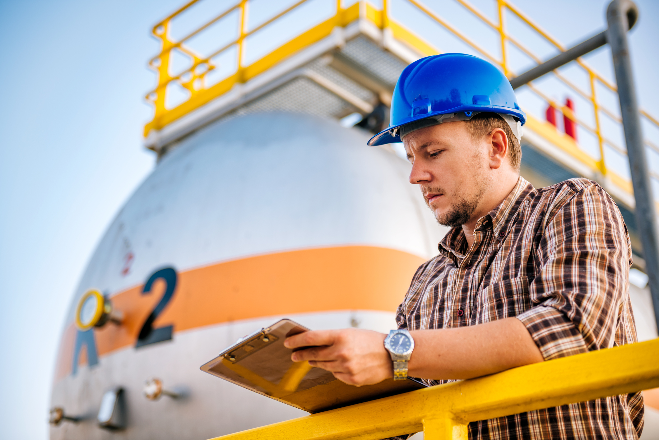 A man with a notebook standing in front of a large propane tank