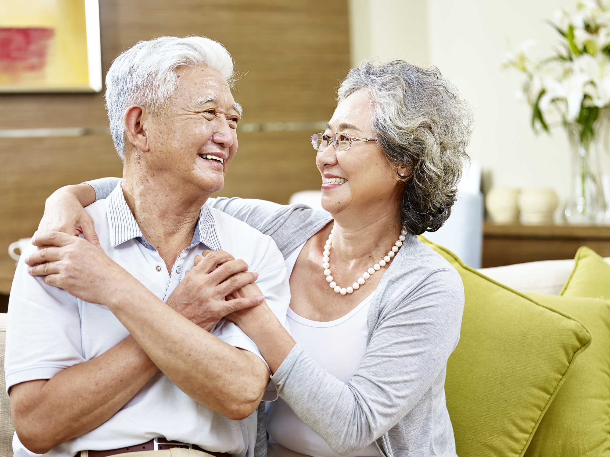 A happy couple with gray hair, with the woman's arms around the man.