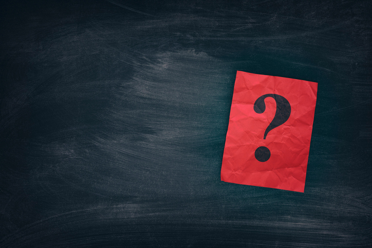 A question mark on a red note card against a chalk board.