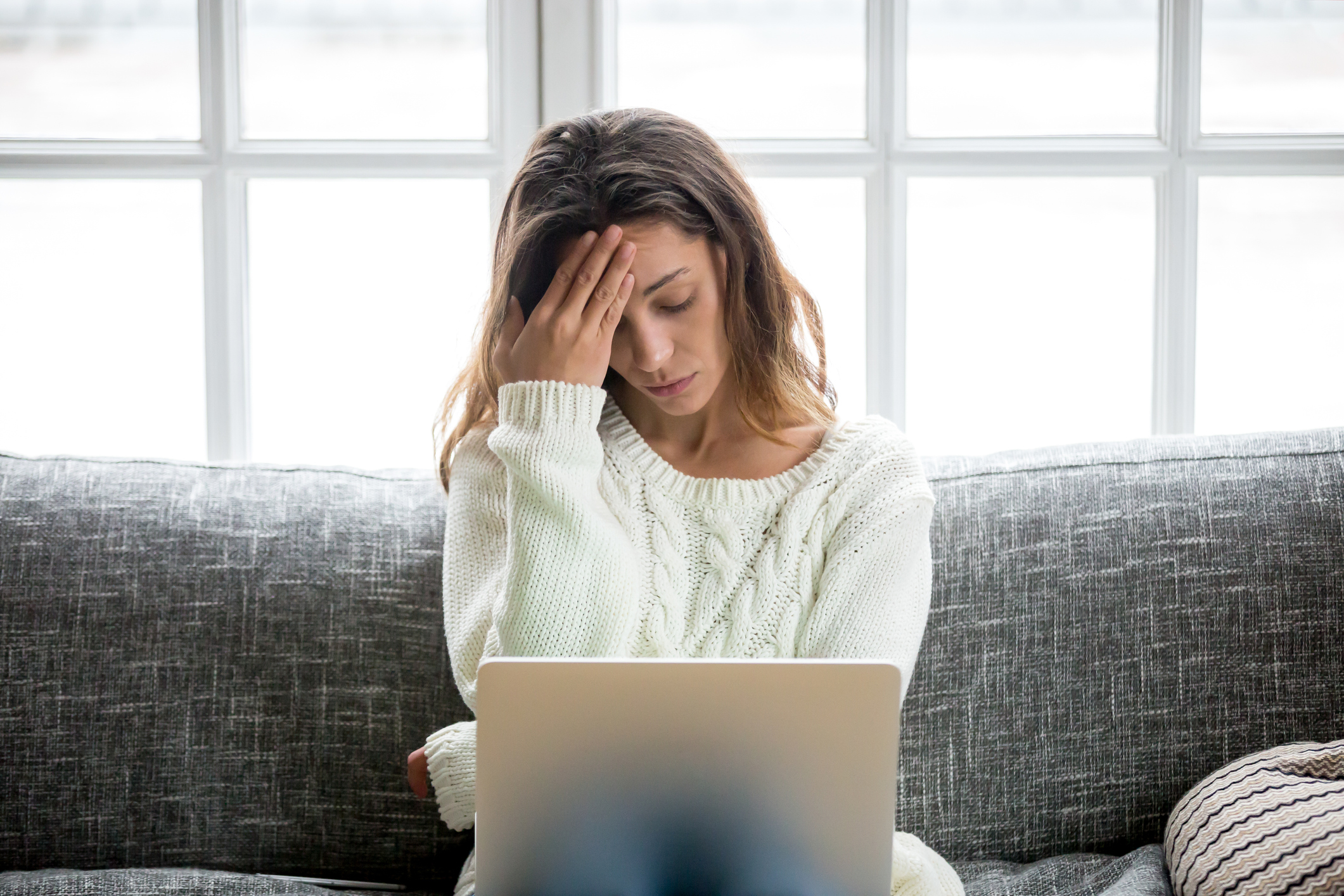 Woman at laptop with her right hand on her forehead