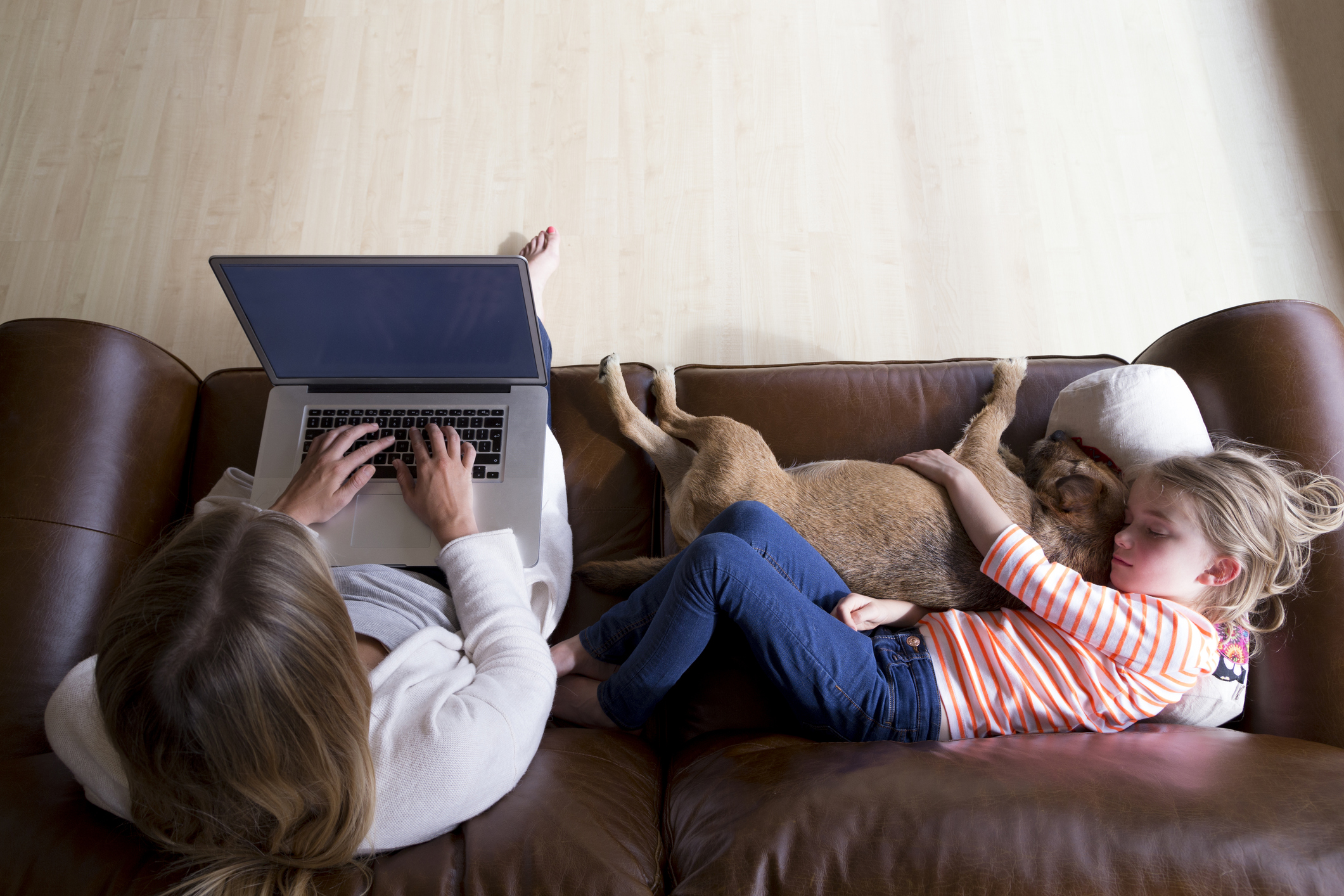 A woman works on a laptop next to a sleeping child.