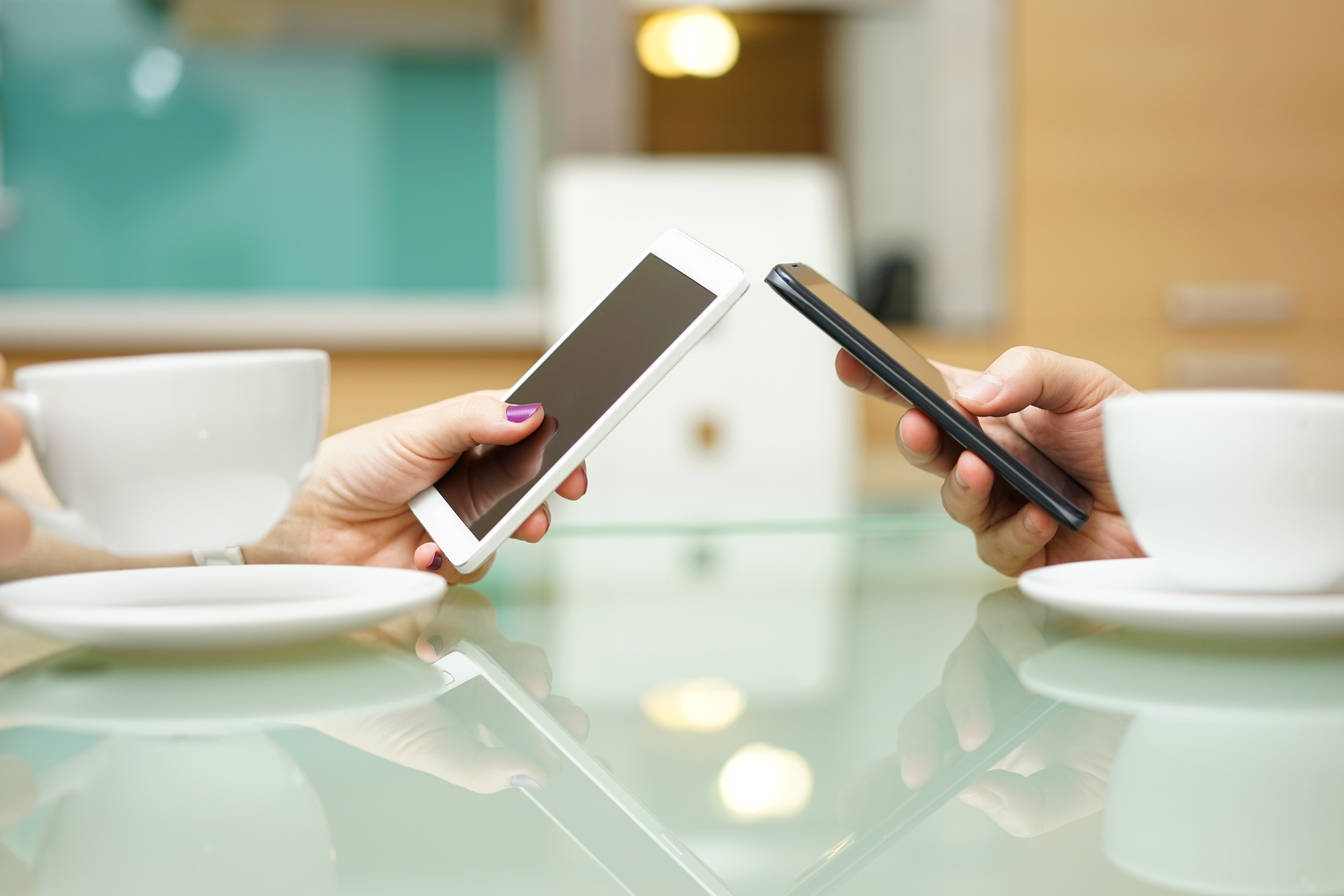 Two people sitting at a table across from each other holding mobile phones