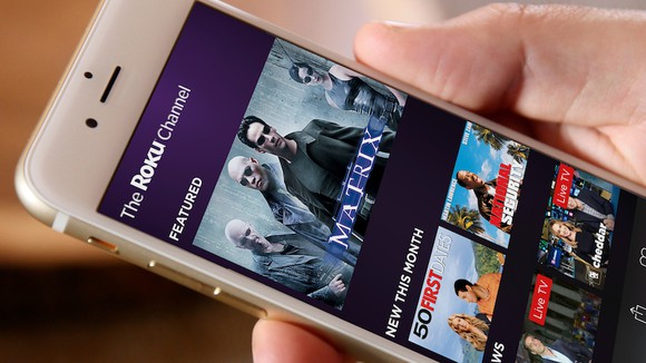 A hand holding a smartphone displaying the Roku app.