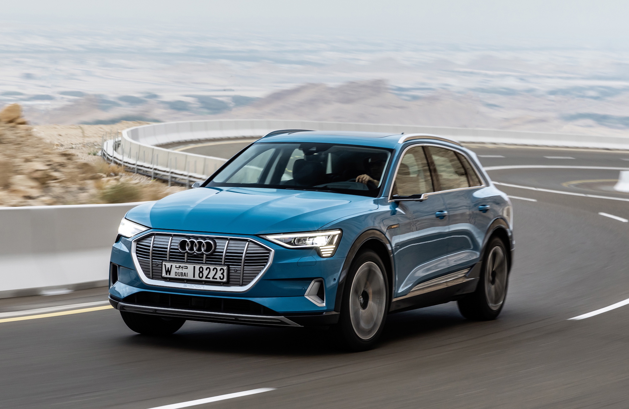 A blue Audi e-tron, a midsize electric luxury SUV, on a curvy road in Dubai.