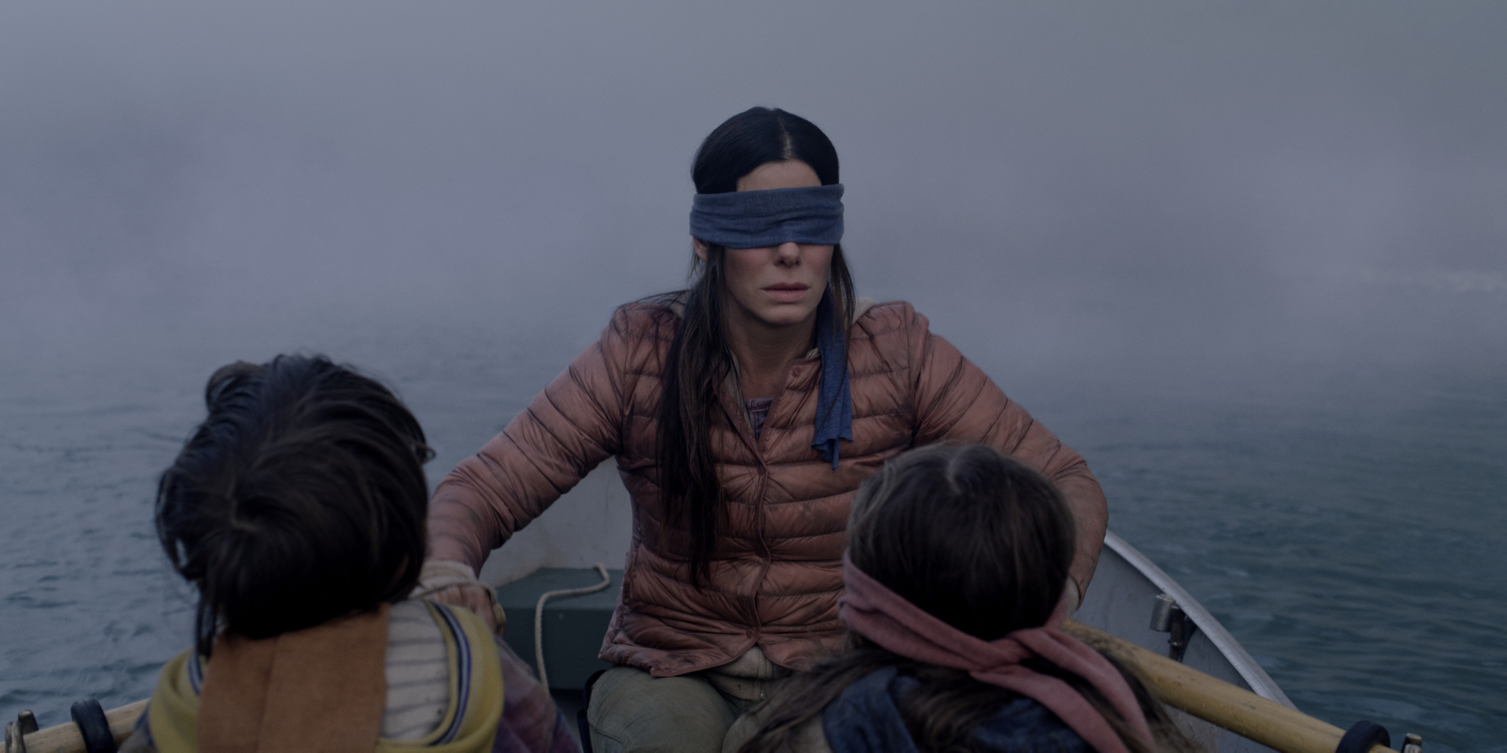 A still from "Bird Box": a woman wearing a blindfold rowing a rowboat with two blindfolded children