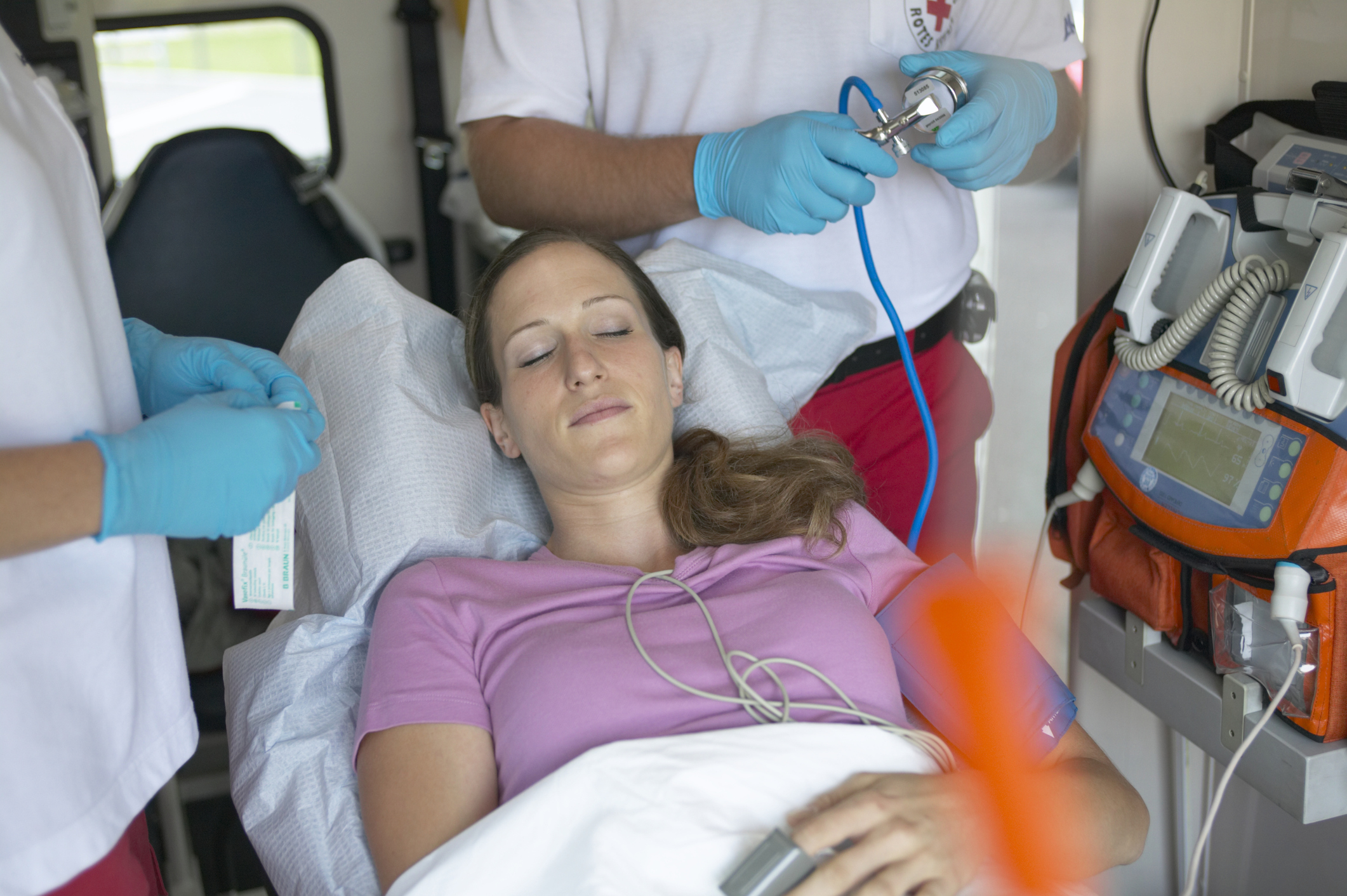 Woman lying down in an ambulance, being tended to by men wearing white shirts and blue gloves