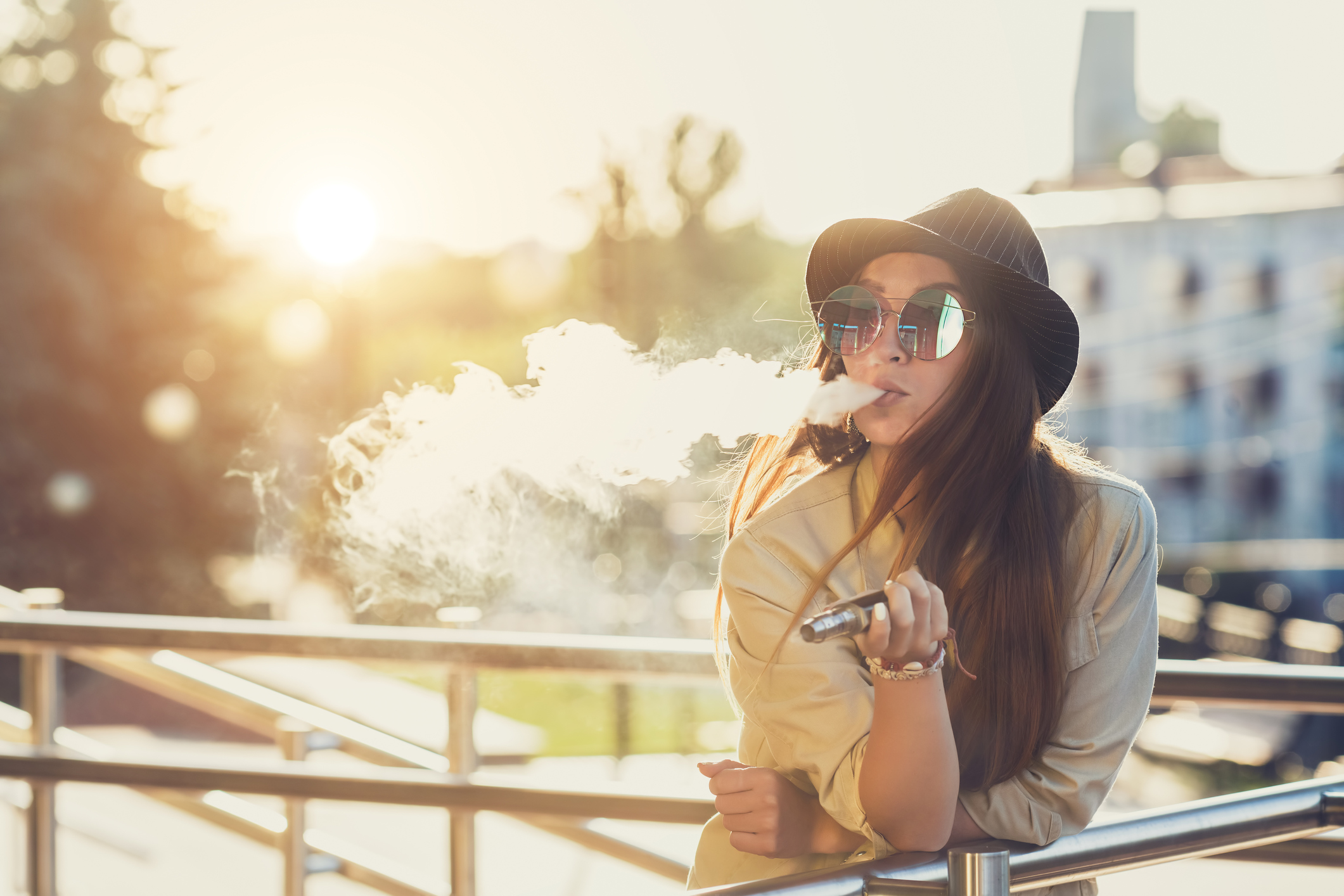 A young woman leaning on a railing while she exhales vapor while vaping