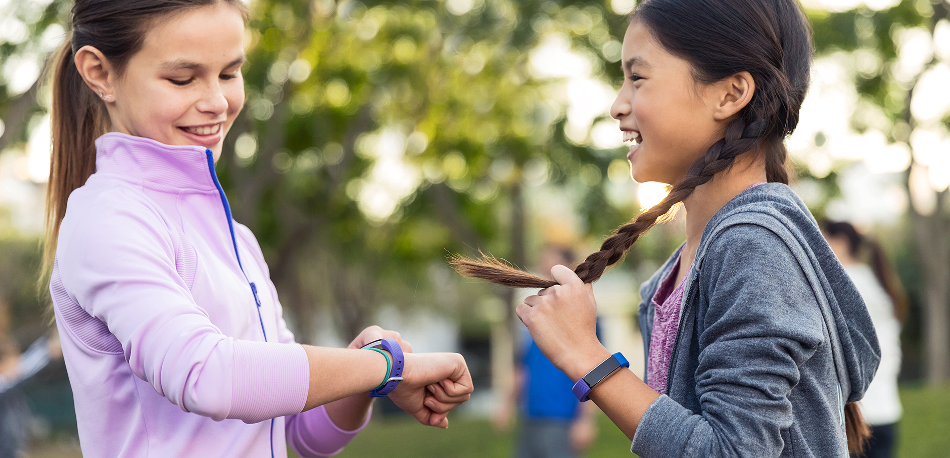 Two young girls laughing and prominently wearing fitness tracker watches.