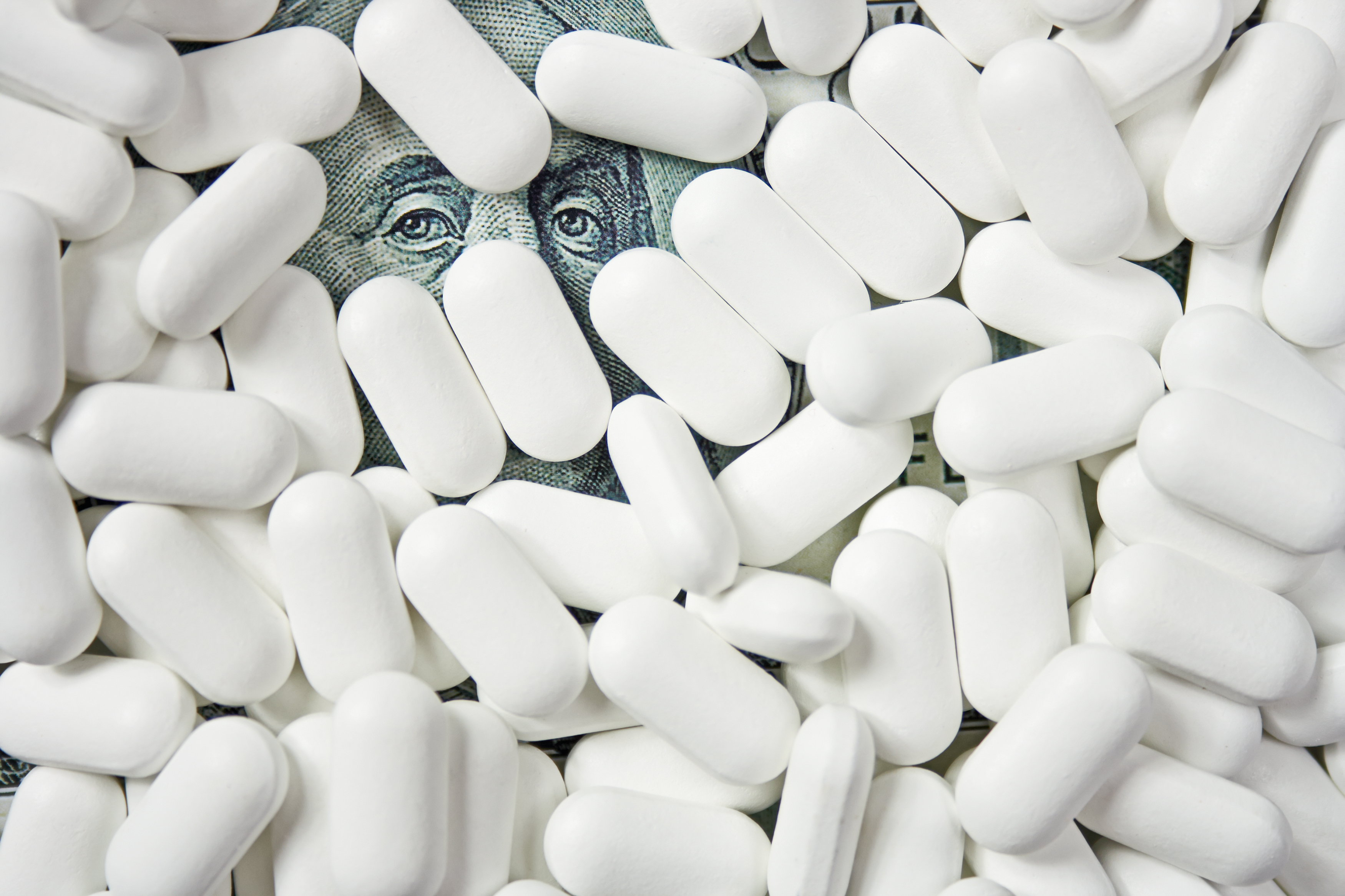 Ben Franklin's eyes on a hundred-dollar bill peeking out from beneath white pills.