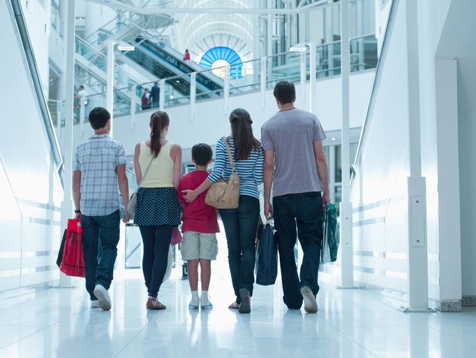 The back view of a man, woman, and three children -- all carrying bags -- as they walk in a shoping mall.