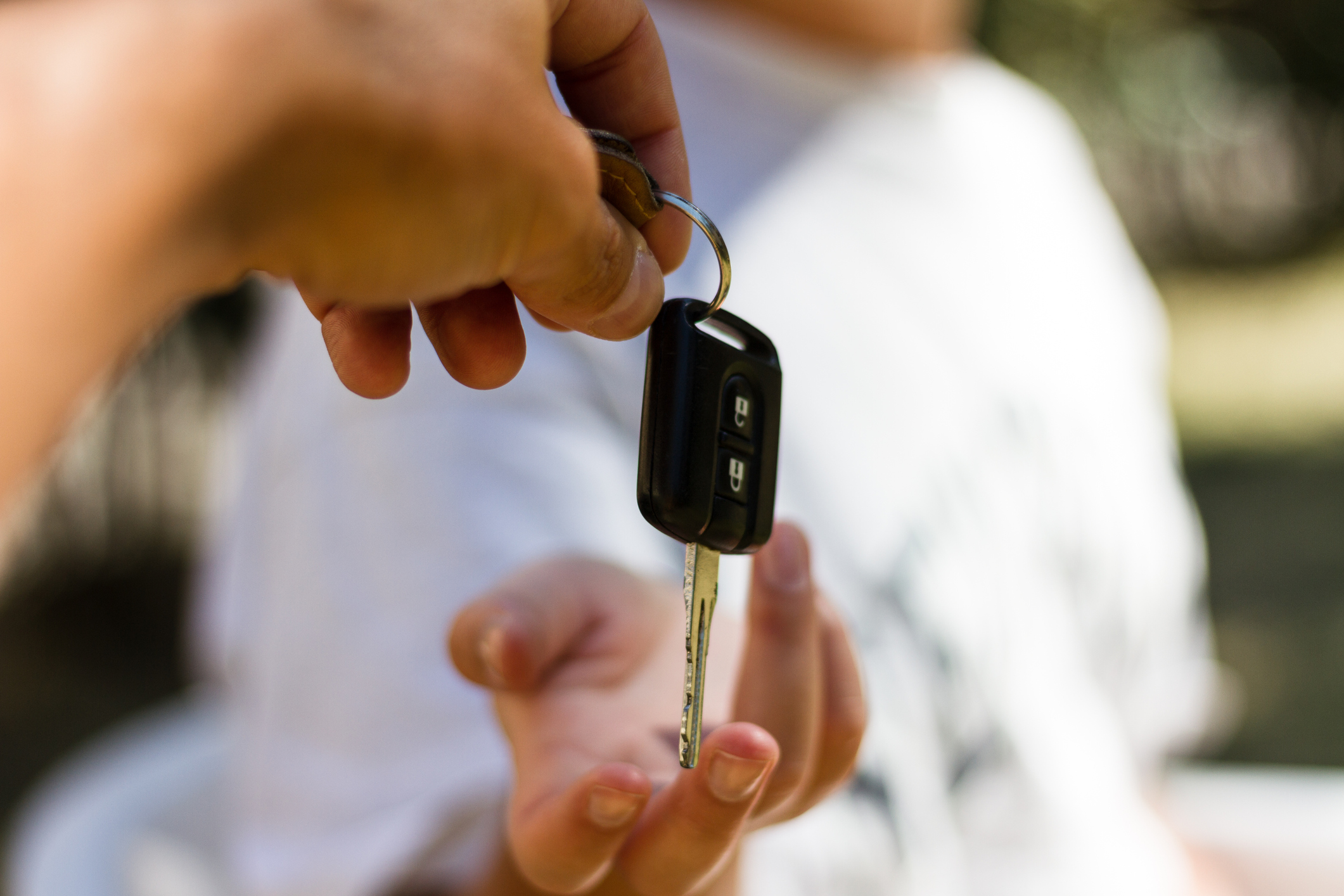 A hand passing a car key to a person in a white shirt.