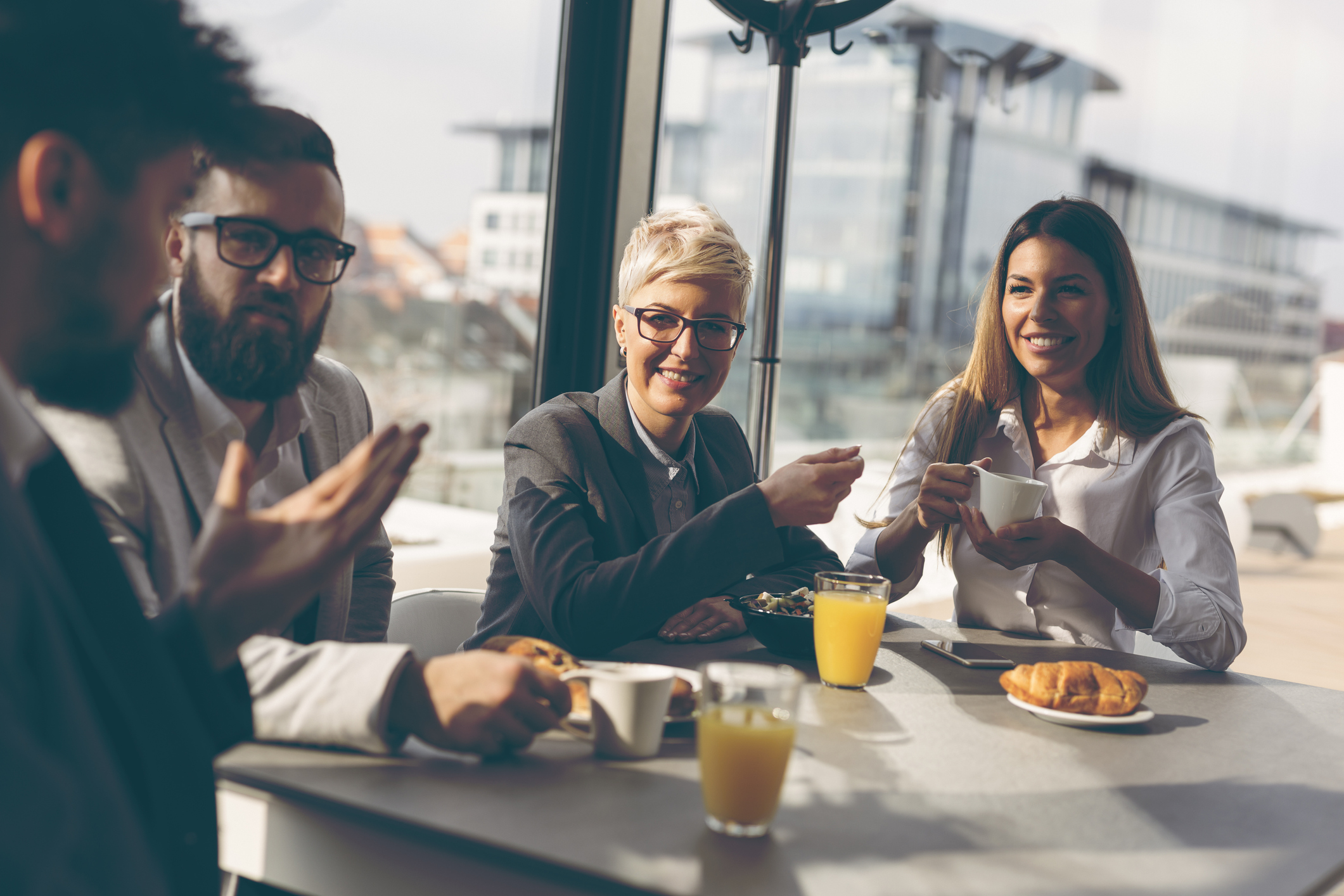 Two professionally dressed men and two professionally dressed women at a table with breakfast items.