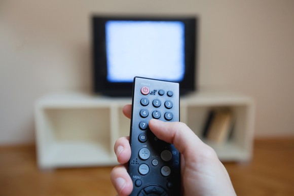 A close-up of a hand holding a TV remote with a static-filled television in the background