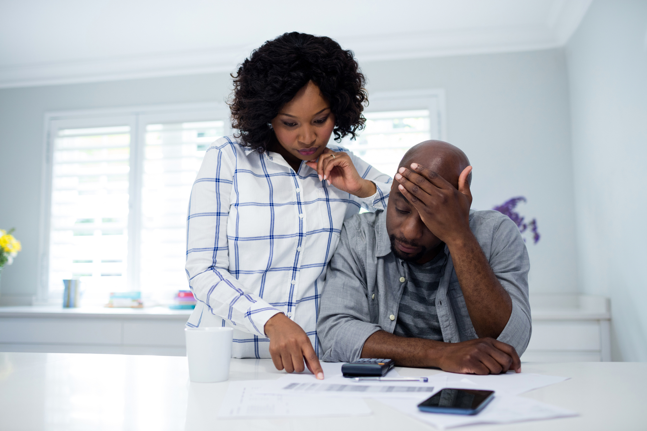 Couple with worried expressions looking at papers with calculators nearby