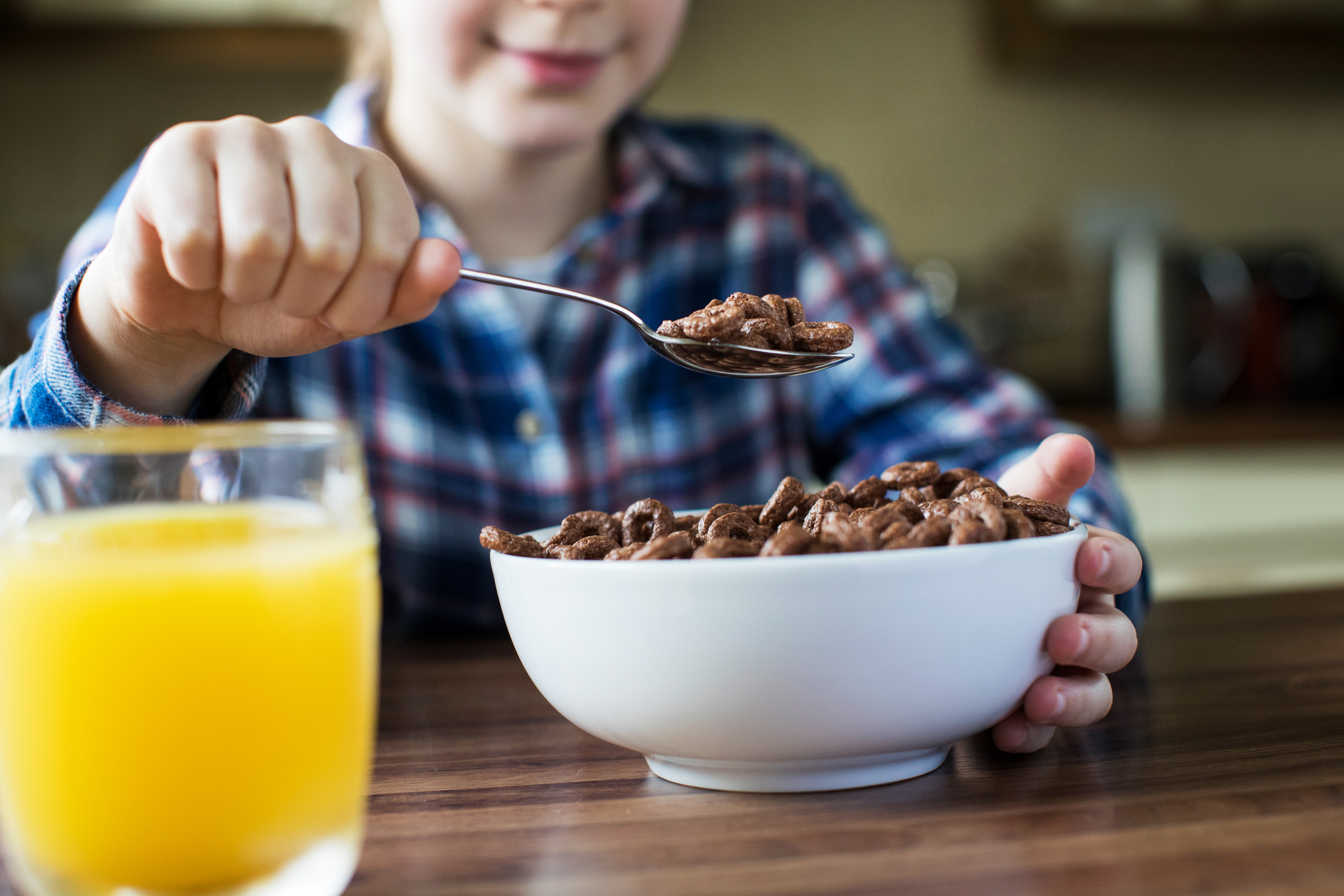 A young girl holding up a spoonful of breakfast cereal at a kitchen table, with a glass of orange juice in front of her.
