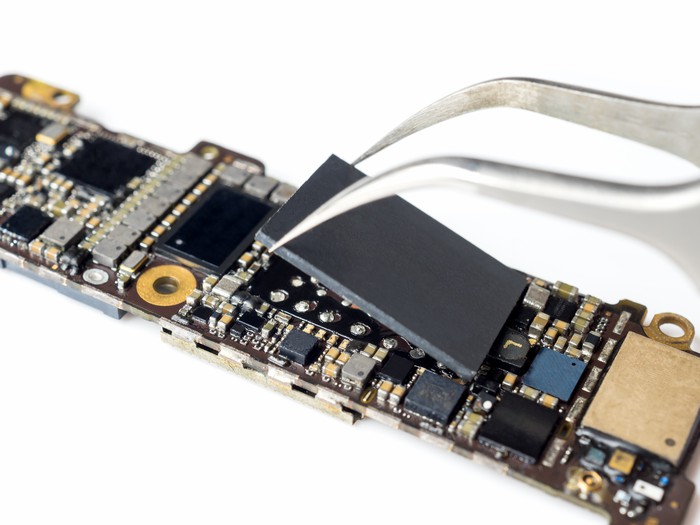 A pair of pliers removing a chip from a logic board.