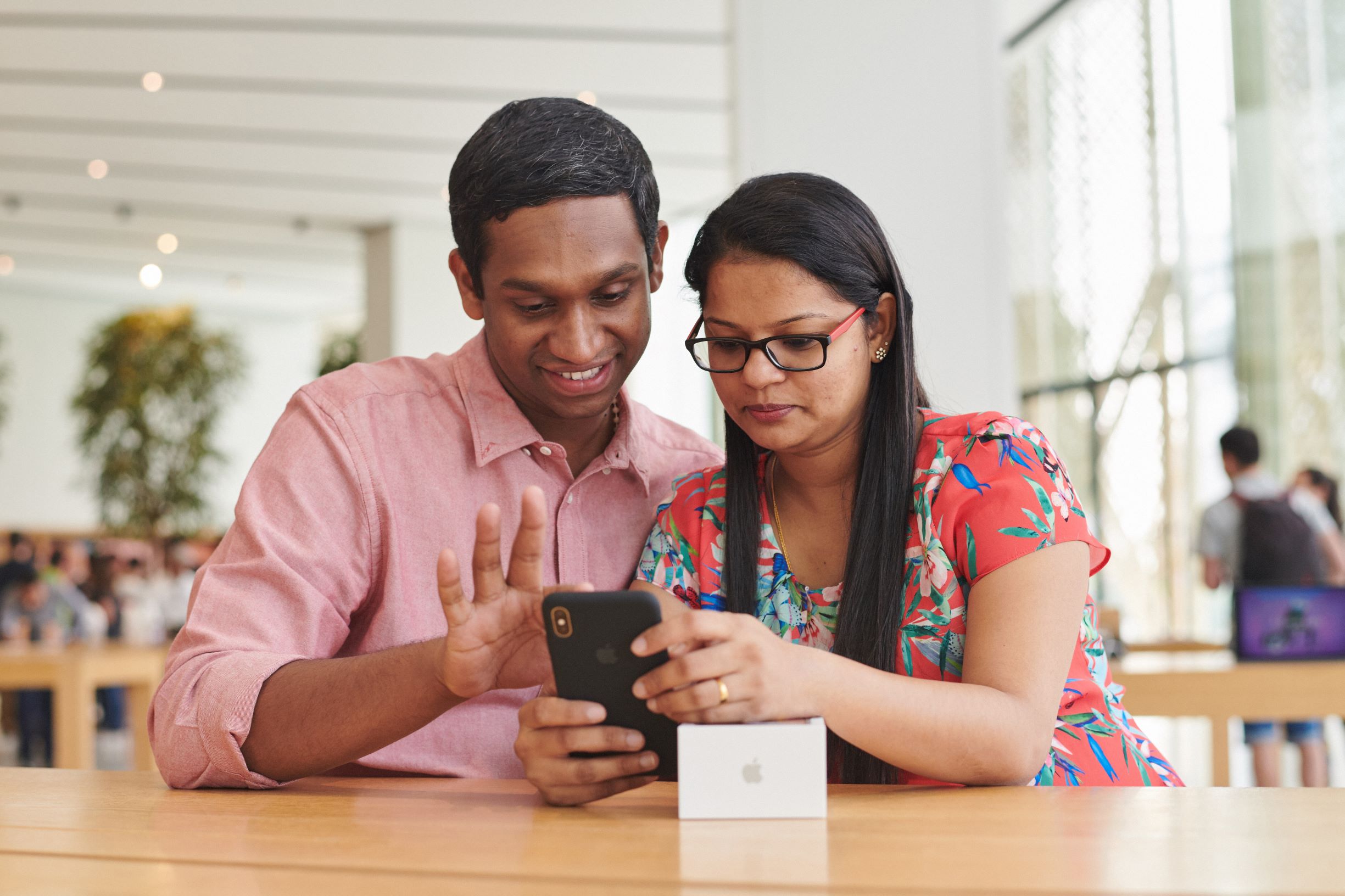 A man and a woman using an iPhone at a wood table in an Apple store.