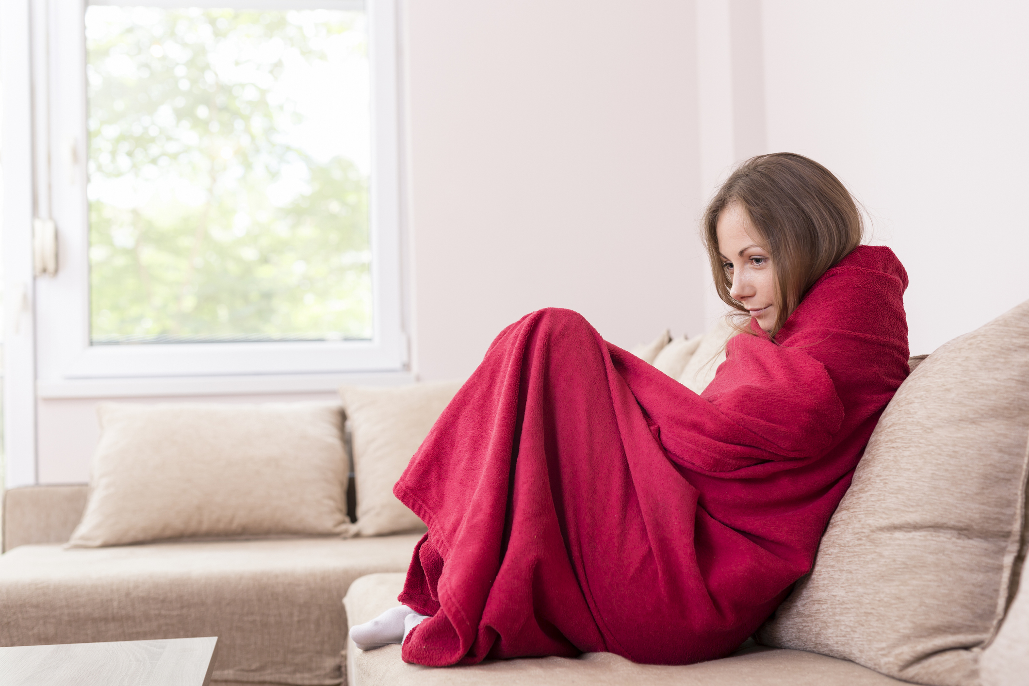 Woman on couch wrapped in a red blanket