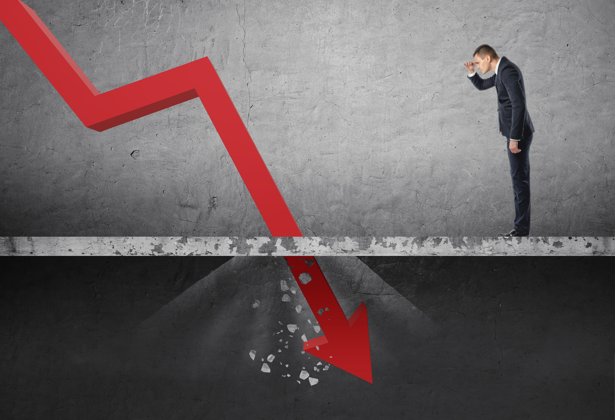 Man in suit watching red arrow chart crash through a concrete floor