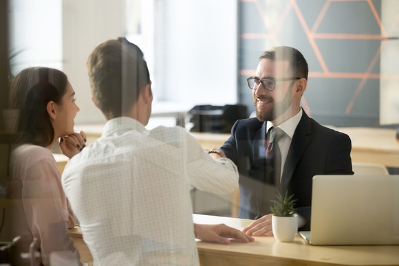 A banker at his desk shakes hands with two customers.