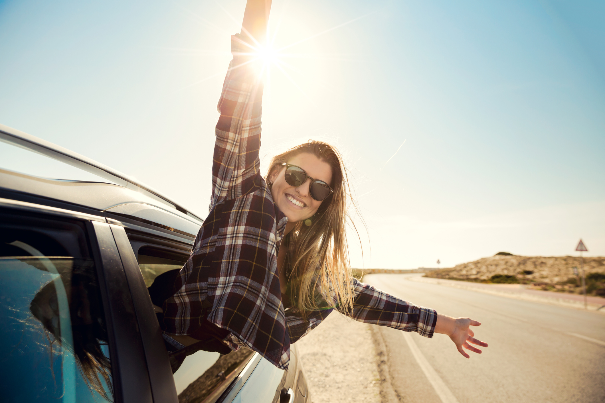 Young woman sticking body out of car window and waving hands in the air