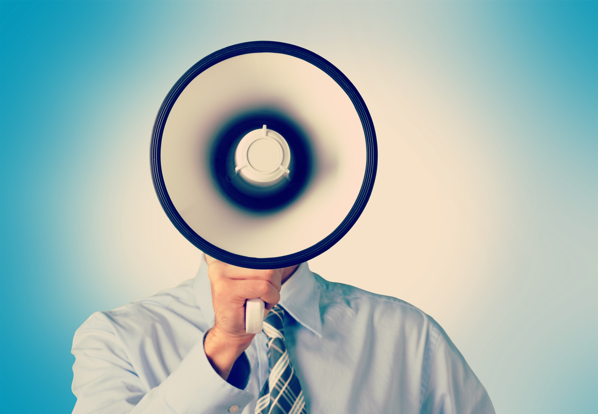 A bullhorn blocks a man's head from our view as he holds it to his mouth.