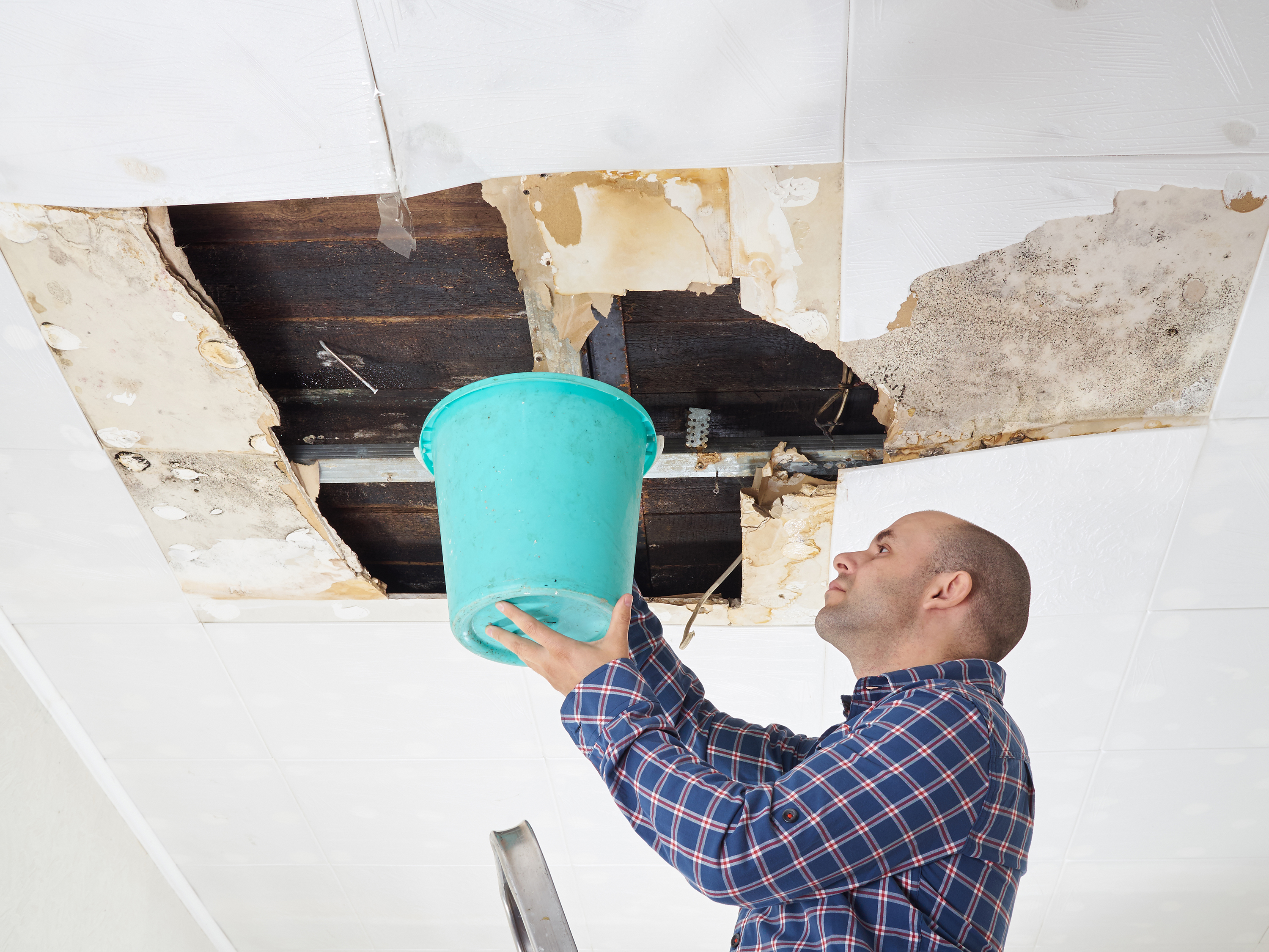 Man holding large bucket up to damaged ceiling