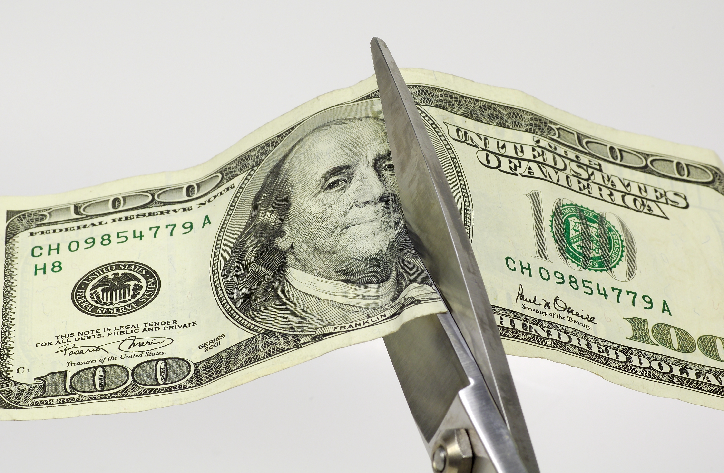 Sissors cutting into a $100 bill.