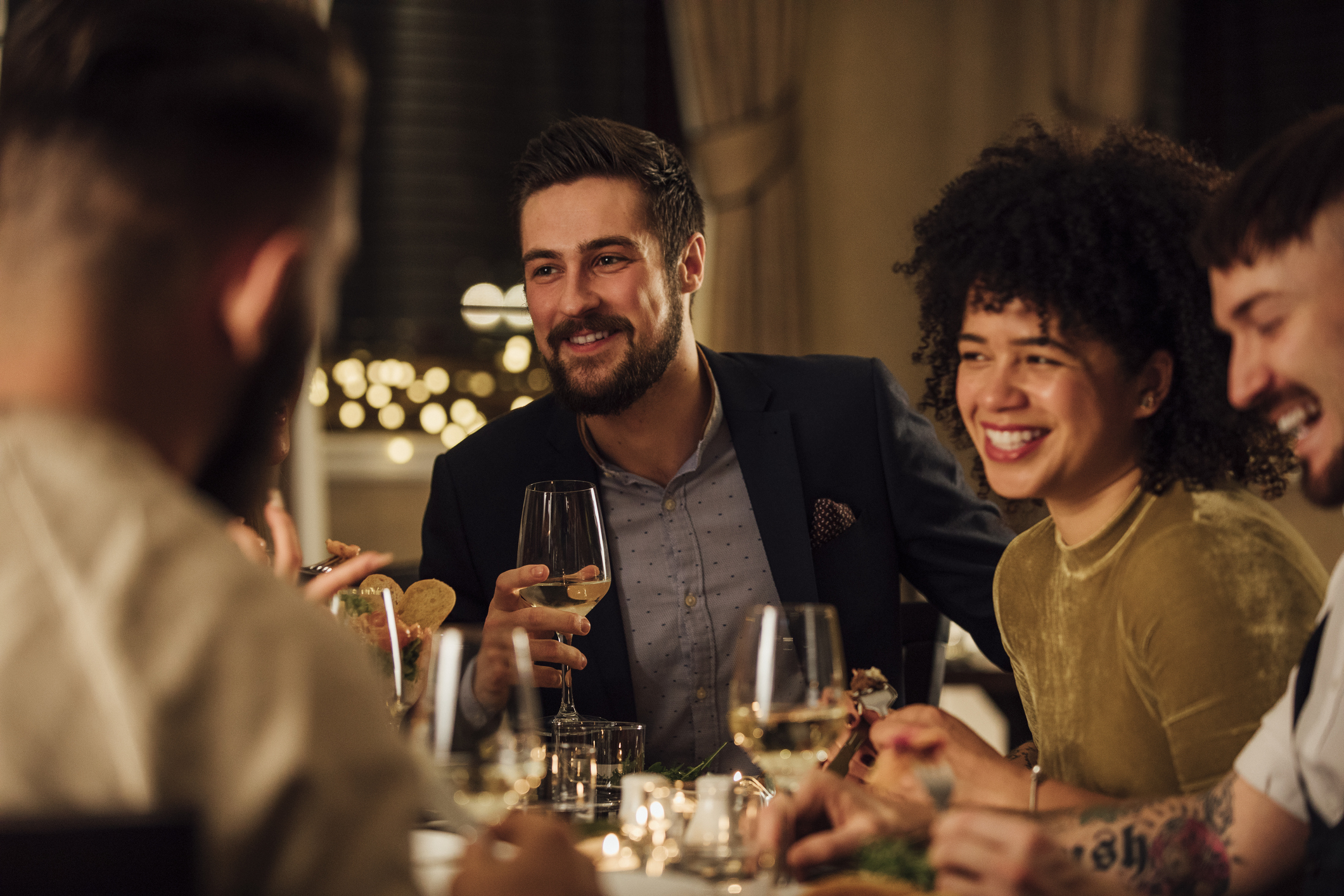 Group of young adults around a table, with wine glasses in hand.