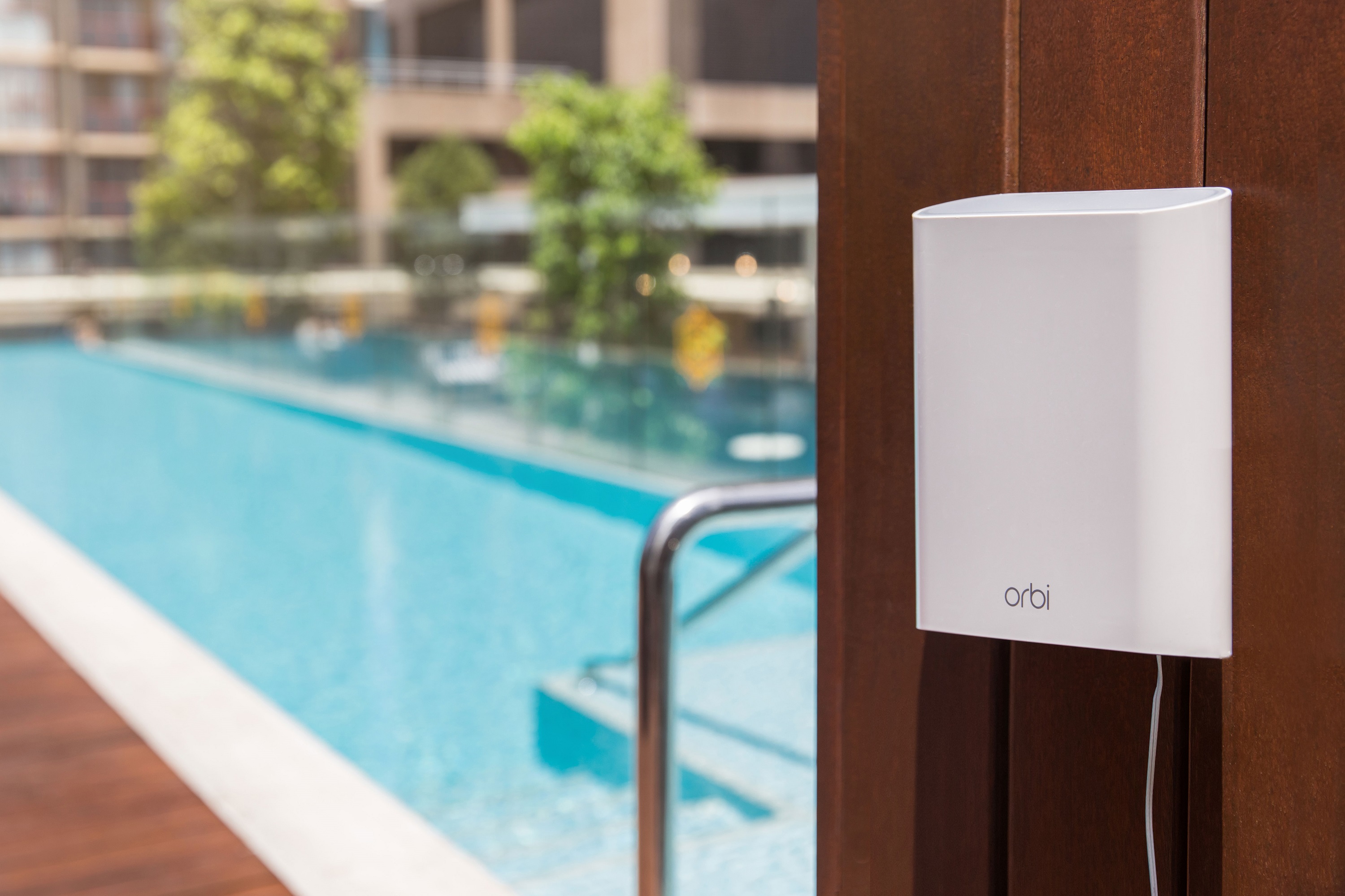 Outdoor Netgear Orbi router mounted on wood wall by pool.