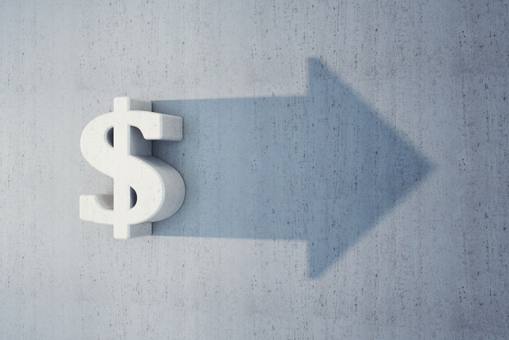 A dollar sign on a wall casting a shadow in the shape of an arrow.