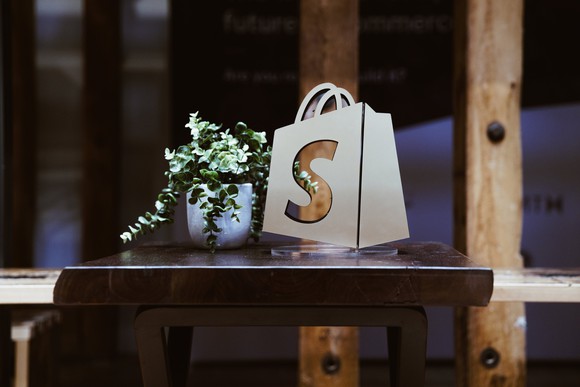 The Shopify logo on a bag, which is sitting on a table next to a plant.